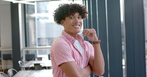 A young man wearing a striped shirt stands confidently in a modern office, exuding professionalism and a sense of self-assurance. This visual is suitable for depicting themes of corporate environments, entrepreneurship, and business settings. It can be effectively used in marketing materials promoting business success, teamwork, office culture, or human resource communications.