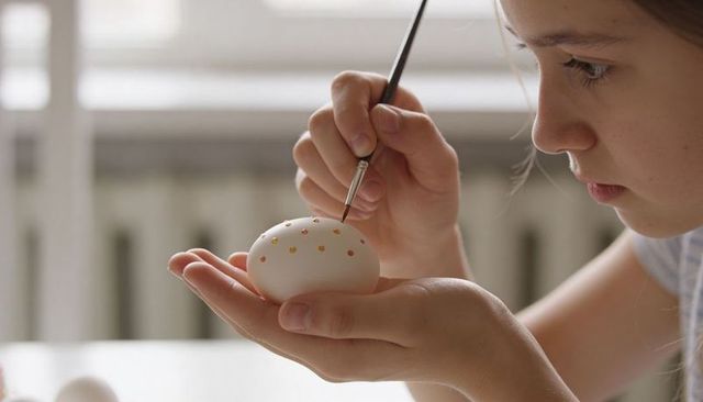 Young girl painting delicate easter egg with fine brush close-up natural daylight