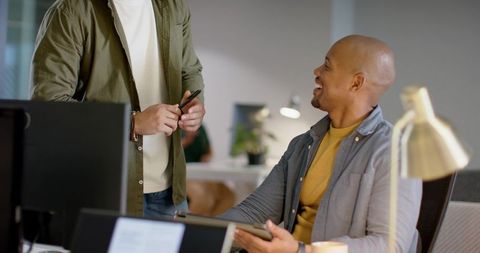 Diverse male coworkers collaborating at modern office desk with tablet and stylus, smiling