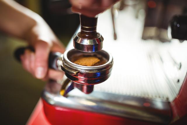 Waitress using a tamper to press ground coffee into a portafilter in cafÃ©