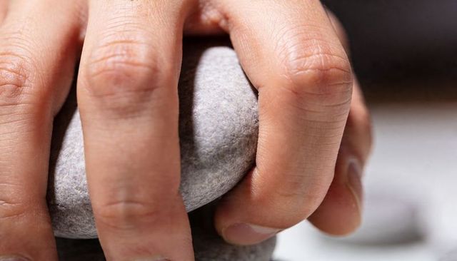 Close-up hand gripping smooth gray pebble for balance, tactile therapy and mindfulness