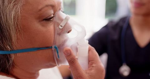 Senior woman using oxygen mask assisted by healthcare professional
