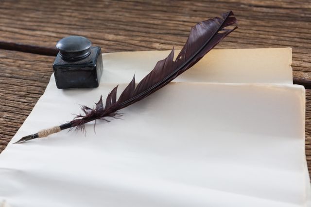 Close-up of quill feather, ink bottle and blank document on wooden table