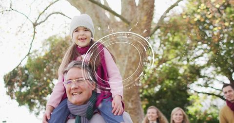 Grandfather carrying granddaughter on shoulders in autumn park, smiling family enjoying moment