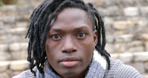 African American man with locs wearing knit sweater and scarf on stone steps portrait