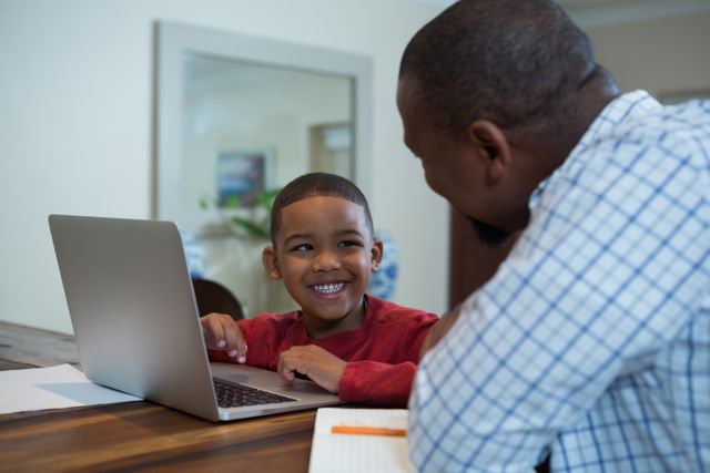 Father and son sharing a tech-savvy moment, enhancing learning and bonding time in comfortable home environment. Perfect for illustrating family technology use, homeschooling, parental involvement, and positive family interactions.