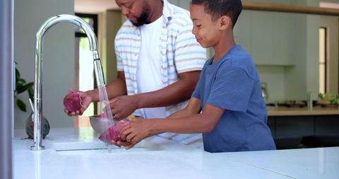African american father and son washing purple vegetables at modern kitchen island