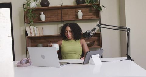 African american woman recording podcast at minimalist home workspace with laptop microphone