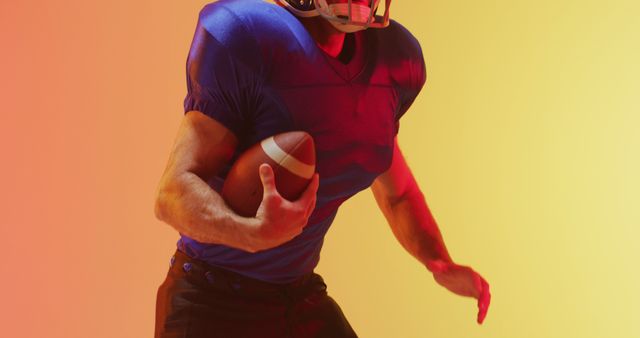 Male American football player wearing blue jersey is running while holding football, set against a vibrant gradient background of yellow and orange hues. Suitable for illustrating sports articles, promoting football events, and in designs emphasizing athleticism and energy.
