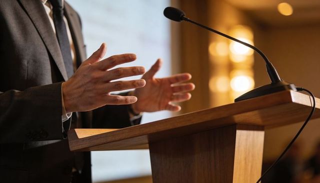 Corporate speaker delivering keynote at wooden podium with expressive hand gestures