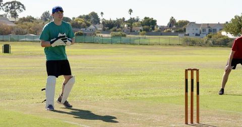 Youth cricket wicketkeeper standing ready on sunny suburban pitch with gloves and pads
