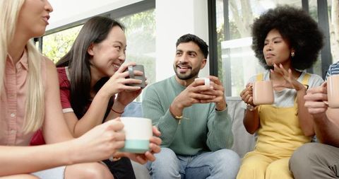 Diverse group of friends socializing on cozy couch with coffee mugs