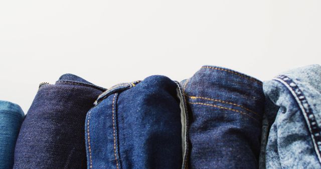 Close-up showing multiple pairs of rolled blue denim jeans against a plain white background. Perfect for fashion websites, clothing store advertisements, or textile industry publications.
