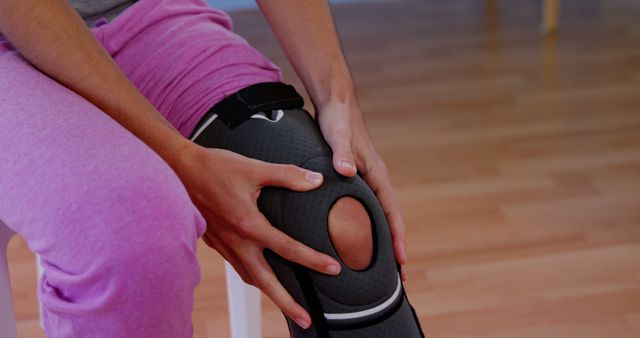 A person is adjusting a black knee brace on their leg, with copy space. Knee braces are commonly used for support during recovery from injuries or to provide stability during physical activities.