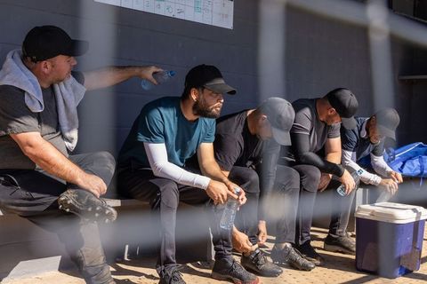 Baseball teammates resting on dugout bench during game break with water bottles
