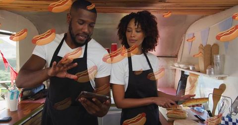 Diverse food truck team preparing hot dog orders while using tablet for mobile ordering