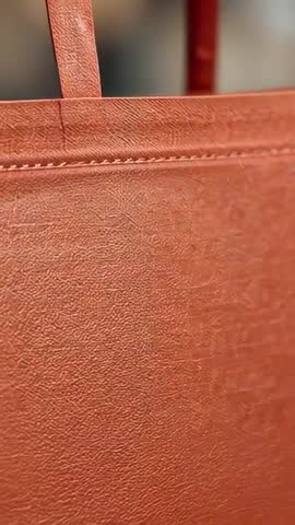 Panning reveal of orange leather tote bag closeup showing strap seam and textured grain