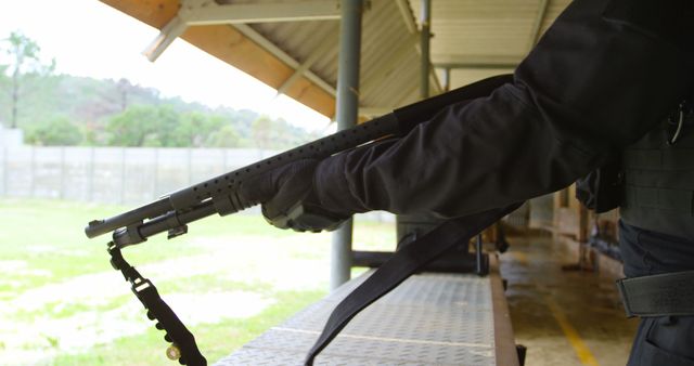 Law enforcement officer holding tactical shotgun outdoors, wearing black tactical gear. Ideal for use in content related to police training, firearm safety, military exercises, security force readiness, law enforcement equipment, and tactical gear. Could be used in articles, security training materials, or promotional content for law enforcement agencies.