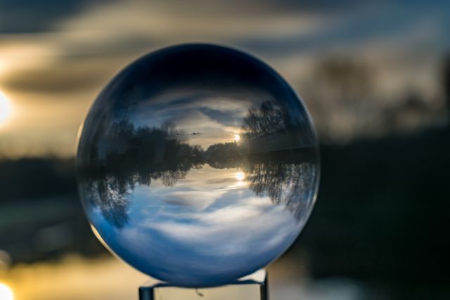 This image captures a mesmerizing sunset as reflected in a glass sphere, with blurred natural landscape in the background. Ideal for use in websites and materials related to nature, meditation, relaxation, environmental conservation, and art. Can also be used as a background for inspirational quotes or as thematic decoration.
