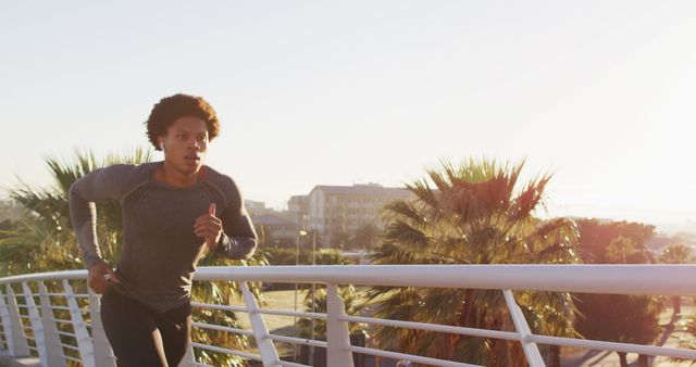Fit african american man exercising outdoors in city wearing earphones, running on footbridge. fitness and active urban outdoor lifestyle.