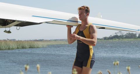 Male Rower Carrying Boat by Riverside Under Sunny Skies - Download Free Stock Images Pikwizard.com
