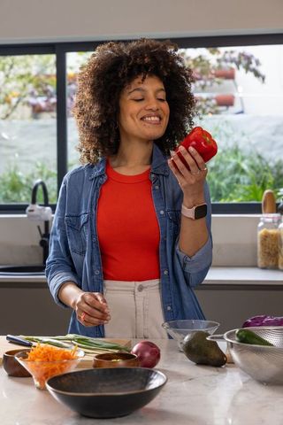 African american woman preparing colorful salad with red bell pepper in bright kitchen