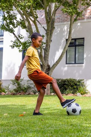 African american boy playing soccer on lawn balancing ball with confident focused pose