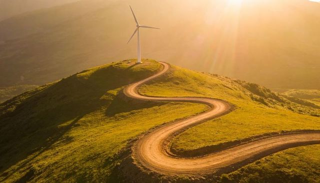 Winding dirt road leading to wind turbine on sunlit hilltop at golden hour