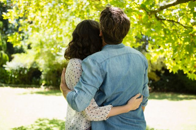 Couple embracing each other in a lush garden on a sunny day. Ideal for use in relationship advice articles, romantic greeting cards, or advertisements promoting outdoor activities and nature retreats.