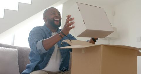 Joyful unboxing at home man lifting white box in sunlit modern minimalist living room