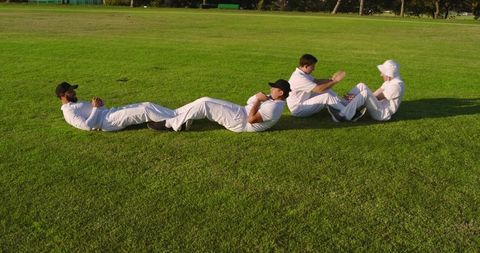 Four cricketers performing partner core exercises on sunlit grass training field
