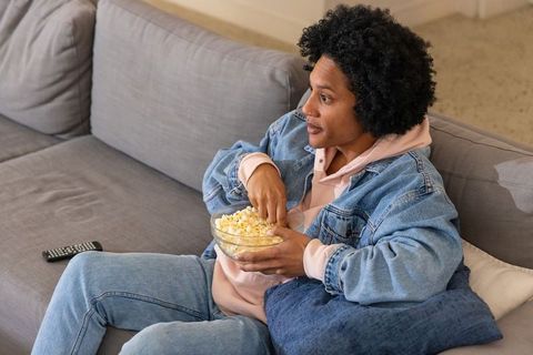 Relaxing african american man on sofa eating popcorn while watching tv at home