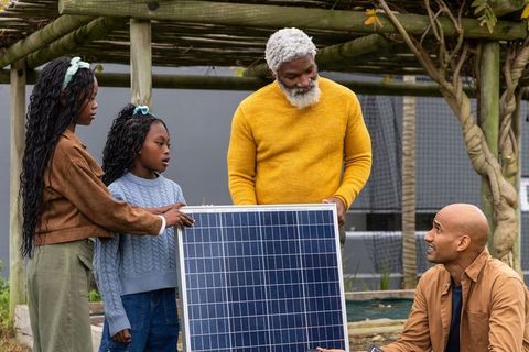 African american family installing solar panel in backyard garden under wooden pergola