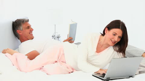 Couple Relaxing in Bed with Laptop and Book