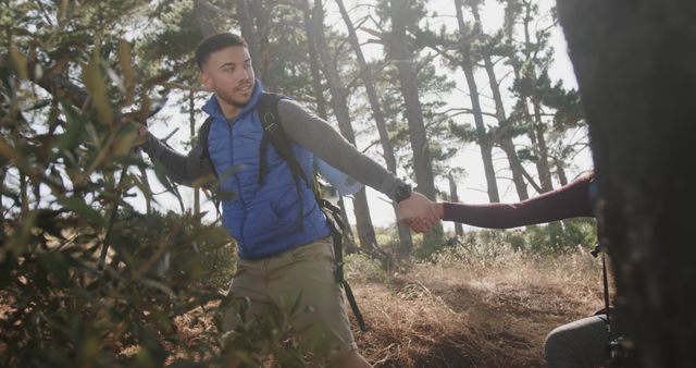 Man leading a friend through a forest while hiking outdoors. The man is wearing outdoor gear and carrying a backpack, showing active lifestyle and adventure. Ideal for use in content about outdoor activities, nature excursions, hiking, camping, teamwork and companionship.