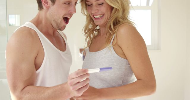 A Caucasian couple, a young man and woman, express excitement while looking at a pregnancy test, with copy space. Their joyful reaction suggests they have received positive news about expecting a baby.