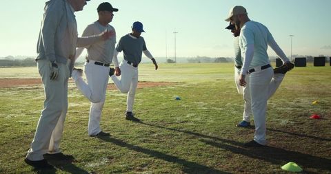 Baseball team stretching morning warmup on grass field wearing caps and gloves