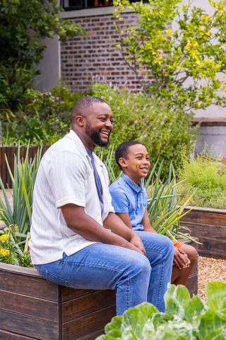 African american father and son sitting on raised planter enjoying frontyard garden