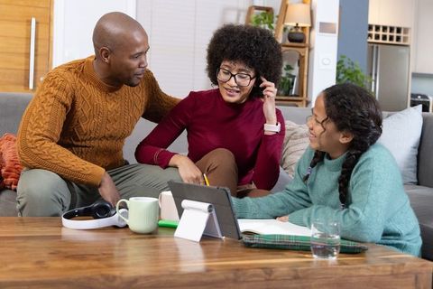 Diverse family helping daughter using tablet on couch for home learning and family bonding