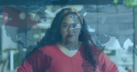 Curly-haired professional standing in open-plan office watching digital world map overlay