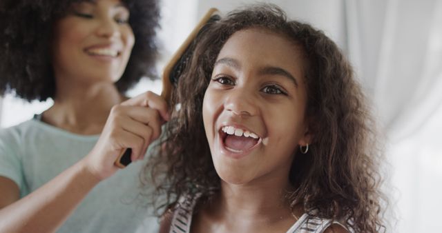 Happy biracial mother and daughter brushing hair with hairbrush. Family, motherhood, childhood, hygene and togetherness, unaltered.