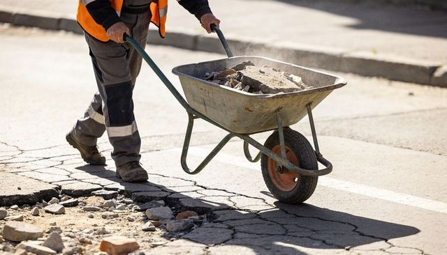 Construction worker pushing wheelbarrow loaded with rubble across cracked urban roadway
