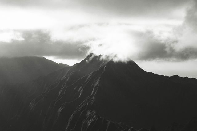 Mountains shrouded in mist at sunrise creates a dramatic and mysterious atmosphere. The black and white tones add a timeless and classic feel. Perfect for themes involving nature, adventure, wilderness, travel, and serene landscapes. Ideal for backgrounds, web design elements, inspirational posters, and travel brochures.