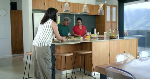 Multi-generational diverse women chopping vegetables and chatting at modern kitchen island