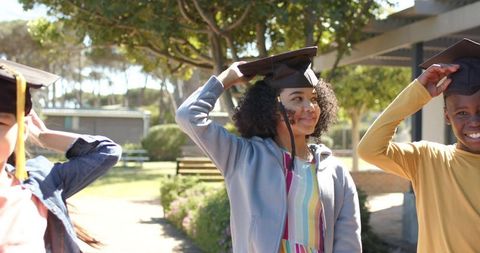 Diverse teens adjusting mortarboards on sunny school campus celebrating graduation