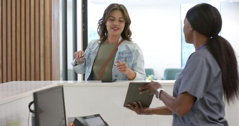 Medical receptionist checking tablet while patient completing digital check-in at modern front desk