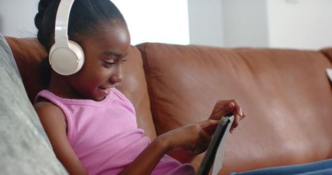 African american girl relaxing at home with tablet and headphones on leather sofa