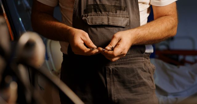 Auto mechanic wearing gray overalls stands in garage, holding tools and equipment. Ideal for promoting automotive services, mechanical repair shops, car maintenance guides, and industrial work environments.