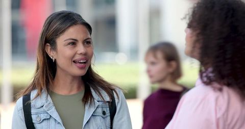 Smiling student starting conversation on campus plaza wearing denim jacket and backpack