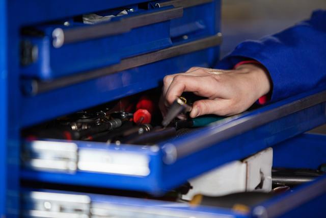 Mechanic hand selecting tools from a blue toolbox drawer in a workshop. Useful for illustrating automotive repair, maintenance services, mechanical work, and tool organization.